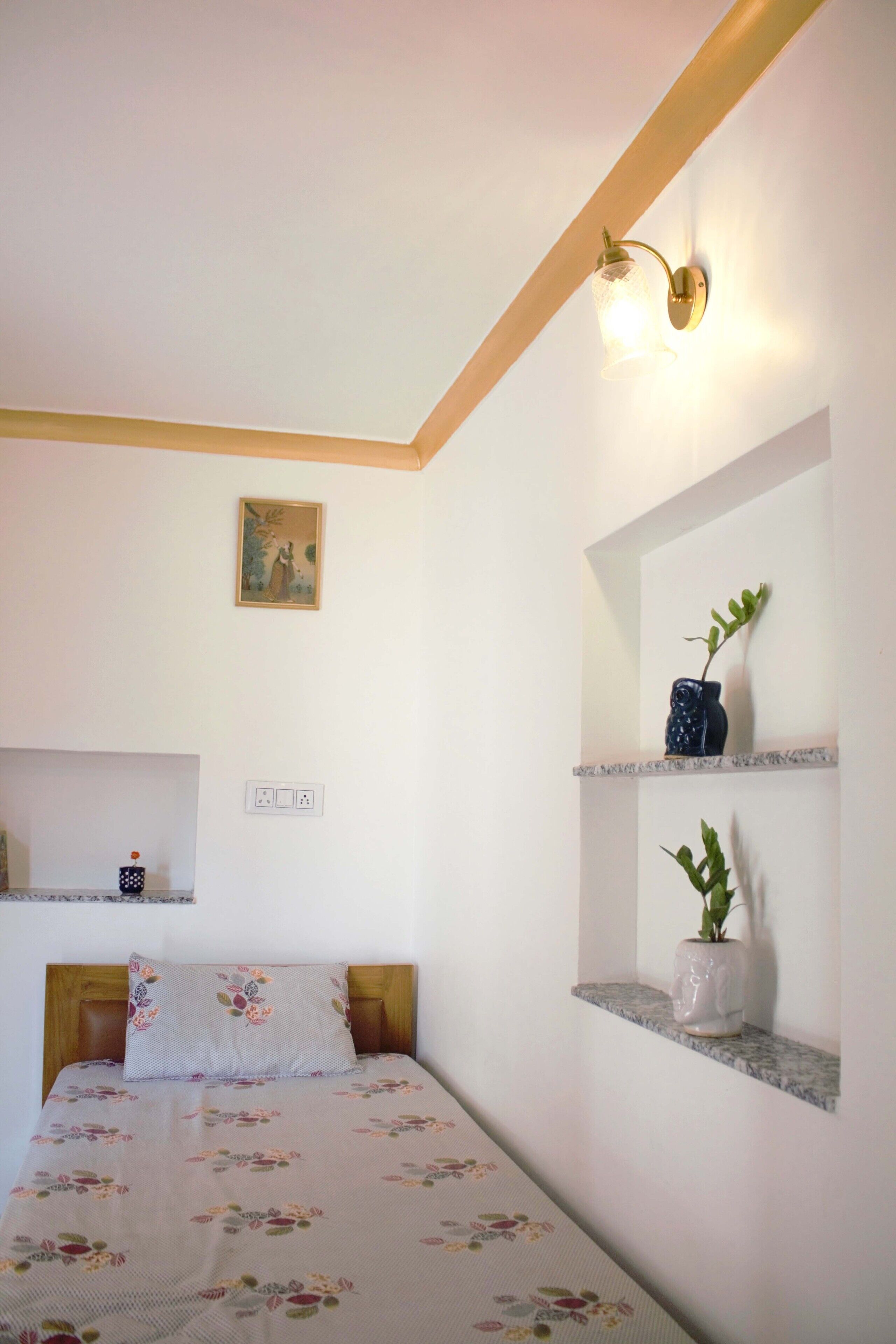 Une chambre à coucher avec un lit, une étagère fixée au mur sur laquelle se trouve un vase, un luminaire fixé au mur et un tableau accroché au mur.