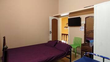A bedroom with a single bed, a green chair, a TV, and a door leading to another room.
