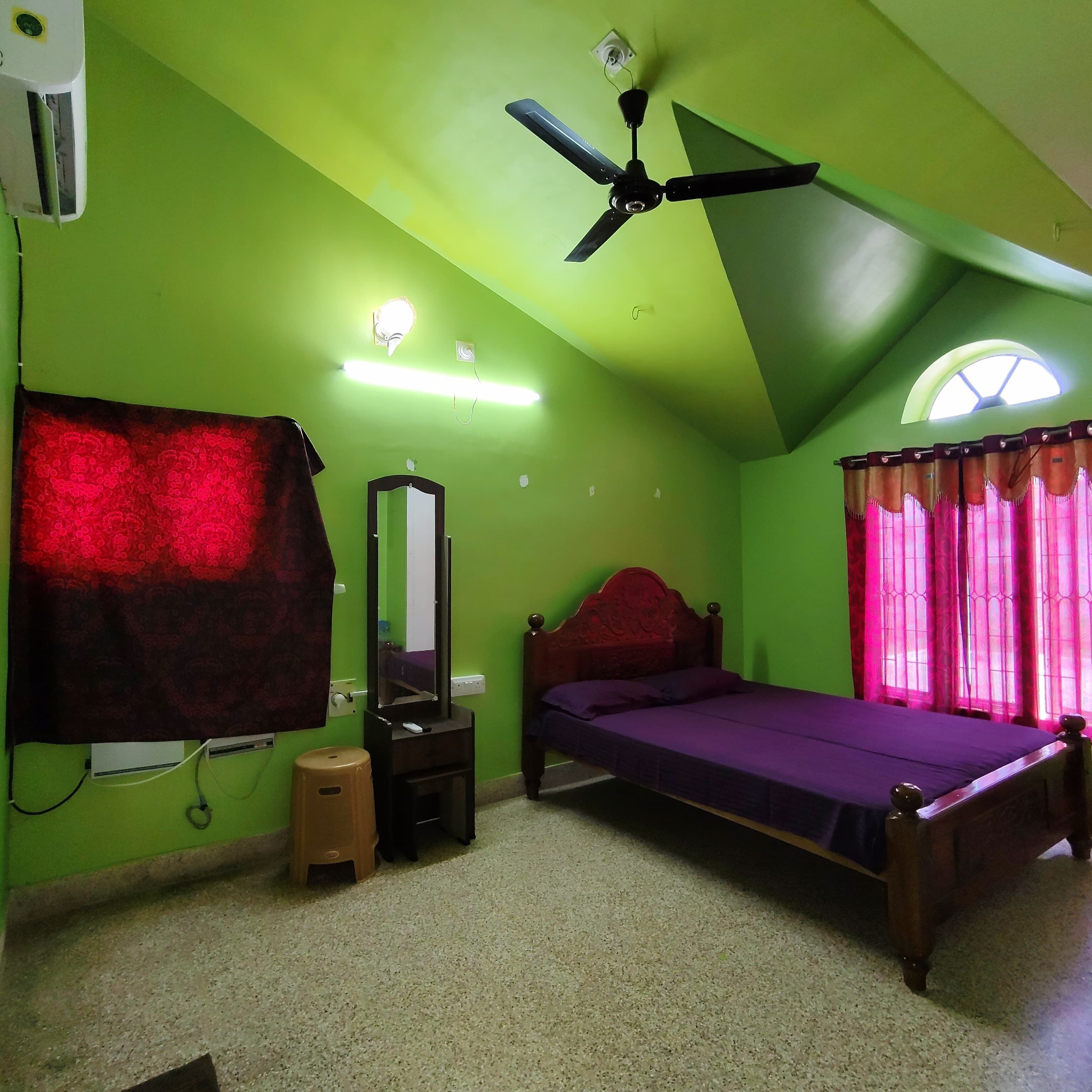 A bedroom with a bed, a ceiling fan, a mirror, and a window with curtains.