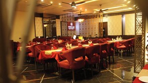 A restaurant with red upholstered chairs and tables, a polished marble floor, and decorative wall panels. - HOTEL RADIANCE PARK RAMPUR (Rampur)