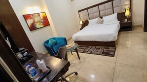 A hotel room with a bed, a desk with a chair, a blue armchair, and a small table. - HOTEL RADIANCE PARK RAMPUR (Rampur)