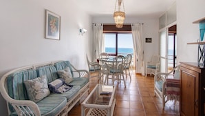 A living room with a sofa, chairs, a table, and a chandelier. - Beachfront T2 Apartment with Sea View and Shared Pool (Quarteira)