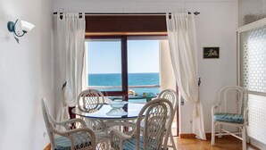 A room with a view of the sea, a dining table with chairs, and a window with curtains. - Beachfront T2 Apartment with Sea View and Shared Pool (Quarteira)