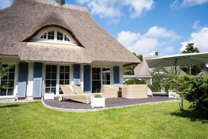 A house with a thatched roof, a covered outdoor seating area with wicker furniture, and a well-maintained lawn.