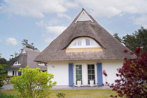 Uma casa tradicional com telhado de palha, telhado triangular, paredes brancas e persianas azuis.