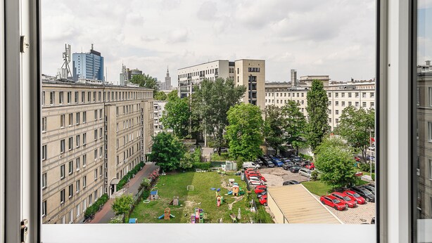 Vista de un paisaje urbano con edificios modernos, un área verde con juegos infantiles y un estacionamiento con coches.