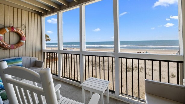 A beach view from a covered balcony with a railing, a small table, and a chair. - Coastal Getaway: Oceanfront Dune King Room (Pawleys Island)