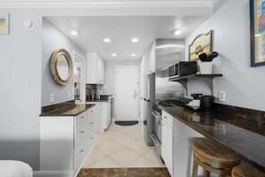 A modern kitchen with white cabinets, a granite countertop, a stainless steel refrigerator, and a microwave.