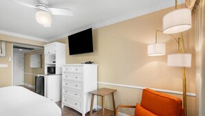 A hotel room with a bed, a desk, a chair, a television, and a kitchenette.