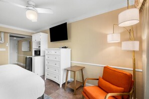 Una habitación de hotel con cama, escritorio, silla, televisor y kitchenette.