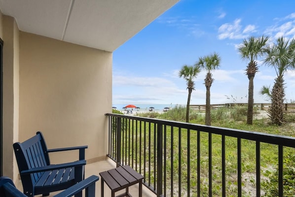 A balcony with a view of the beach, featuring a chair, a small table, and a railing. - Bright and Beautiful Dunes King Room 1st Floor (Pawleys Island)