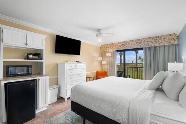 Une chambre d’hôtel équipée d’un lit, d’une télévision, d’un bureau avec une chaise, d’un petit réfrigérateur et d’un balcon avec vue.