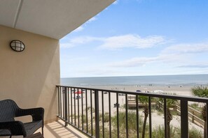 Un balcón con vista a la playa, una silla y una barandilla.
