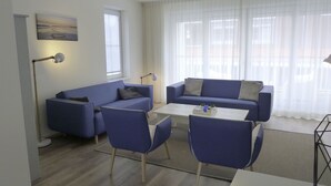 Un salón moderno con un sofá azul, una mesa de centro y sillas a juego. Hay un cuadro en la pared y una lámpara de pie.