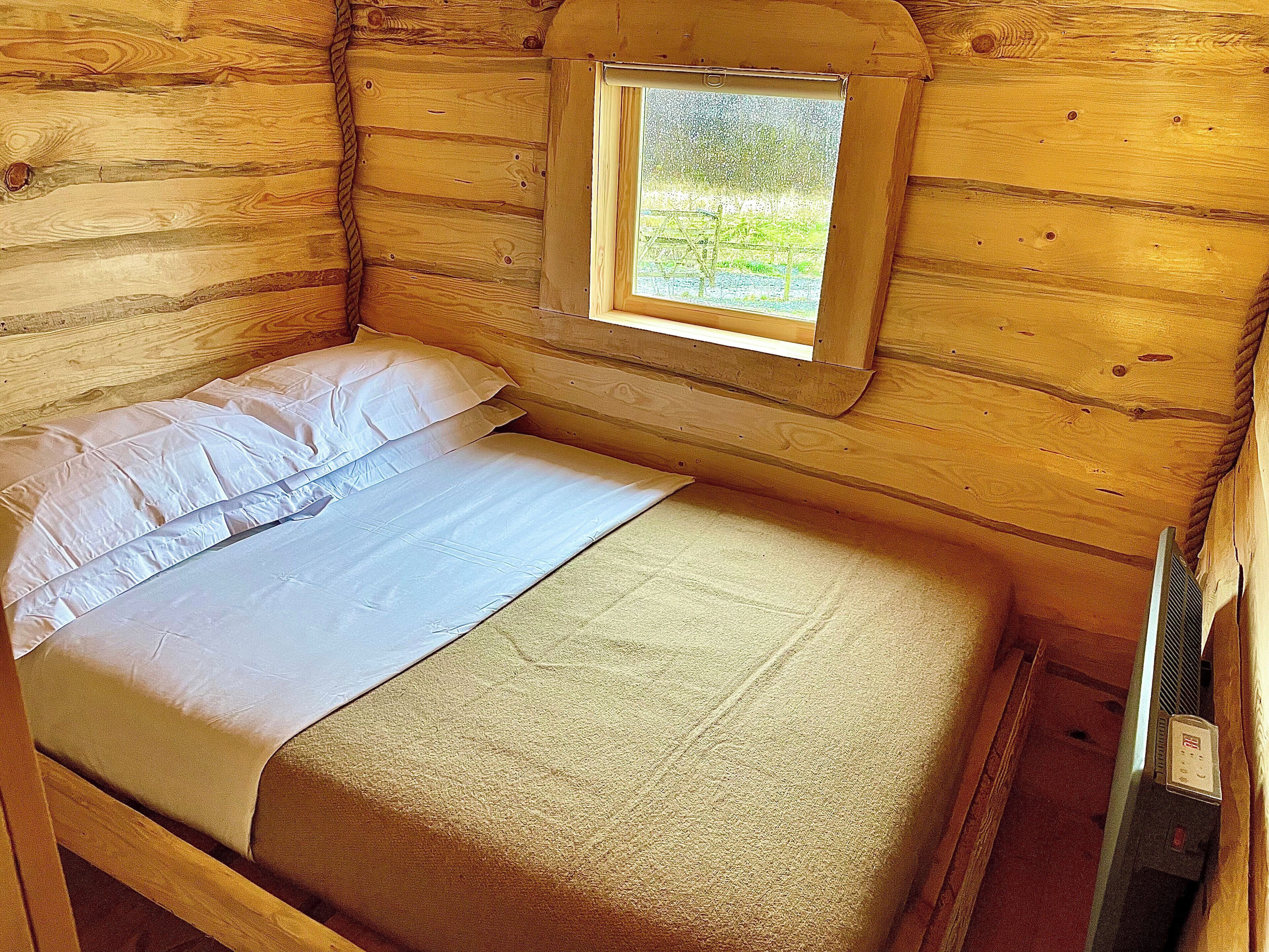 Una habitación de cabaña de madera con una cama, un ventanal y un calentador.