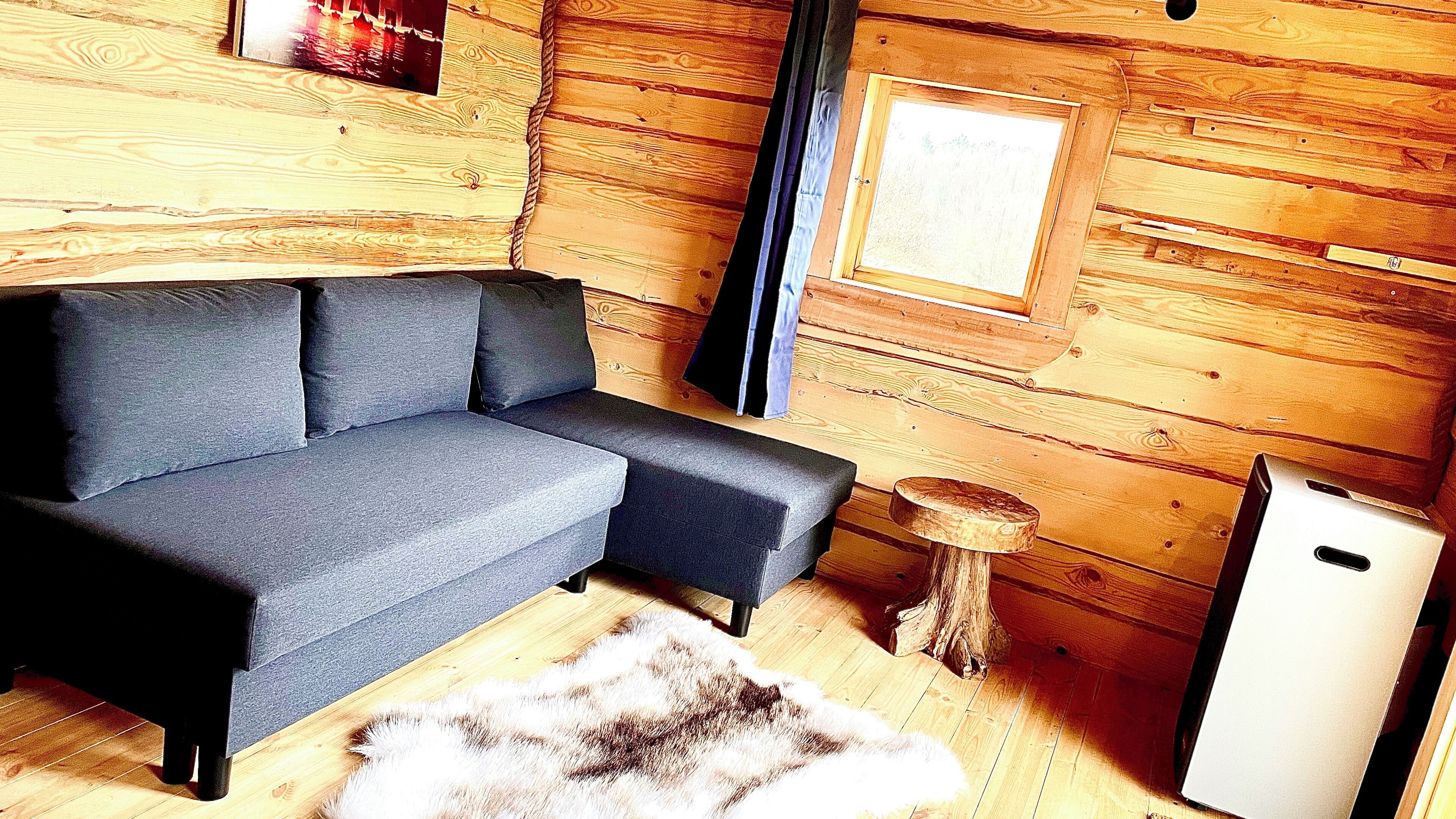 A cozy cabin interior with a grey sofa, a small round table, and a white refrigerator.