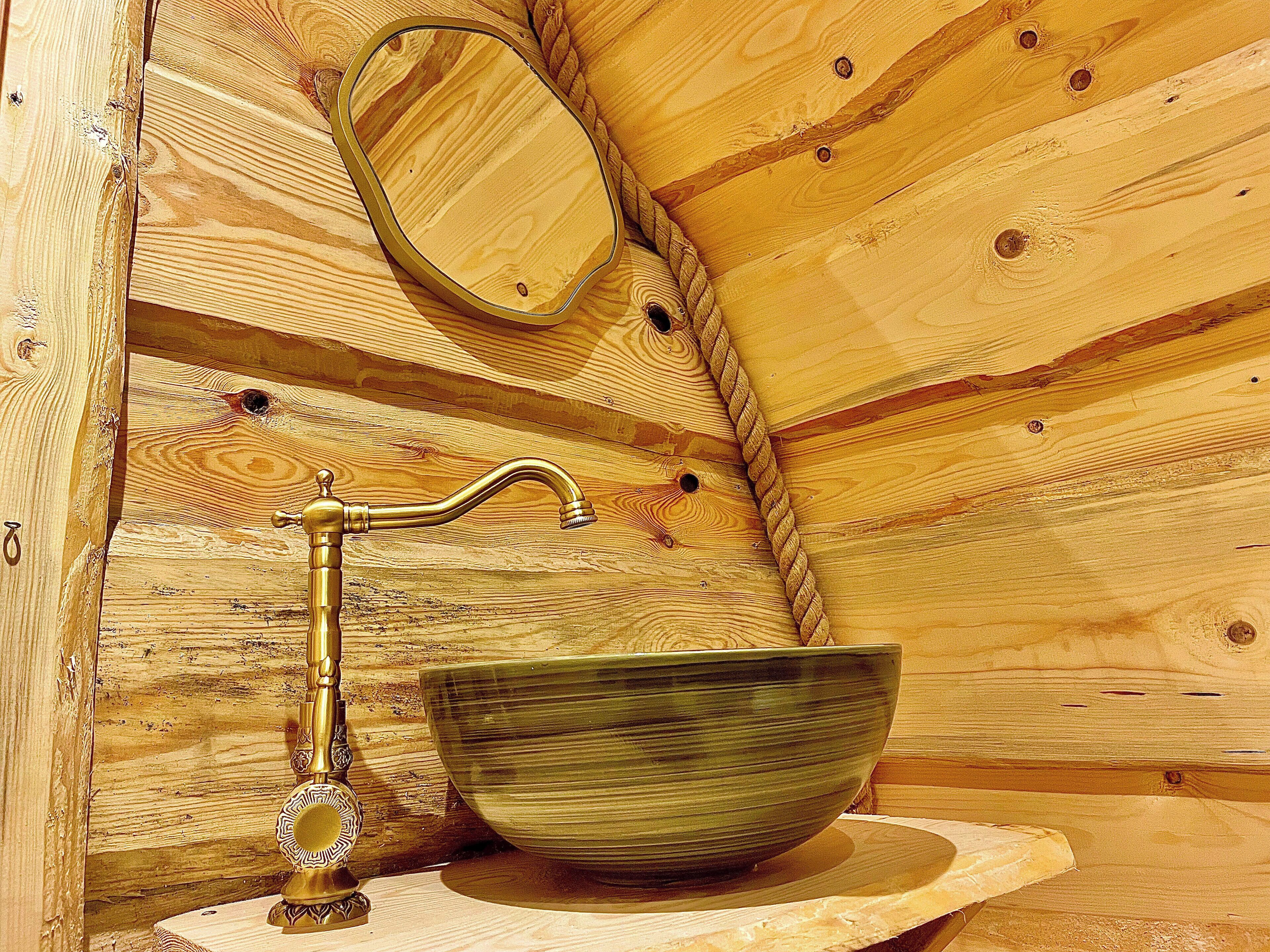 A wooden cabin interior with a wooden sink, a mirror, and a decorative metal faucet.