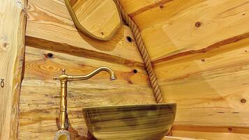 A wooden cabin interior with a wooden sink, a mirror, and a decorative metal faucet.