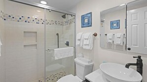 A bathroom with a glass-enclosed shower, white tiles, a white sink, and two blue-framed mirrors. - Beaches and Waves Resort View 2nd Floor (Pawleys Island)