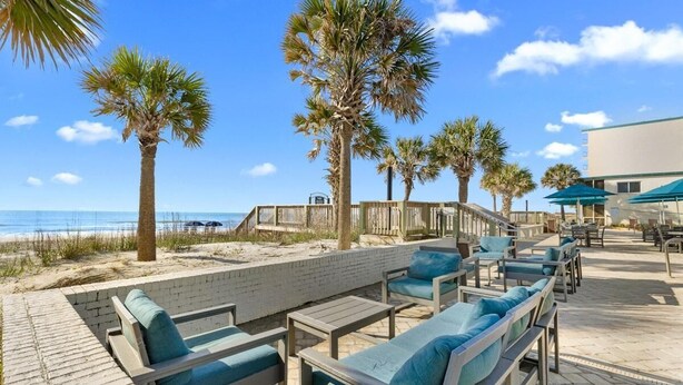 A beachside patio with lounge chairs, a brick wall, and palm trees. - Beaches and Waves Resort View 2nd Floor (Pawleys Island)