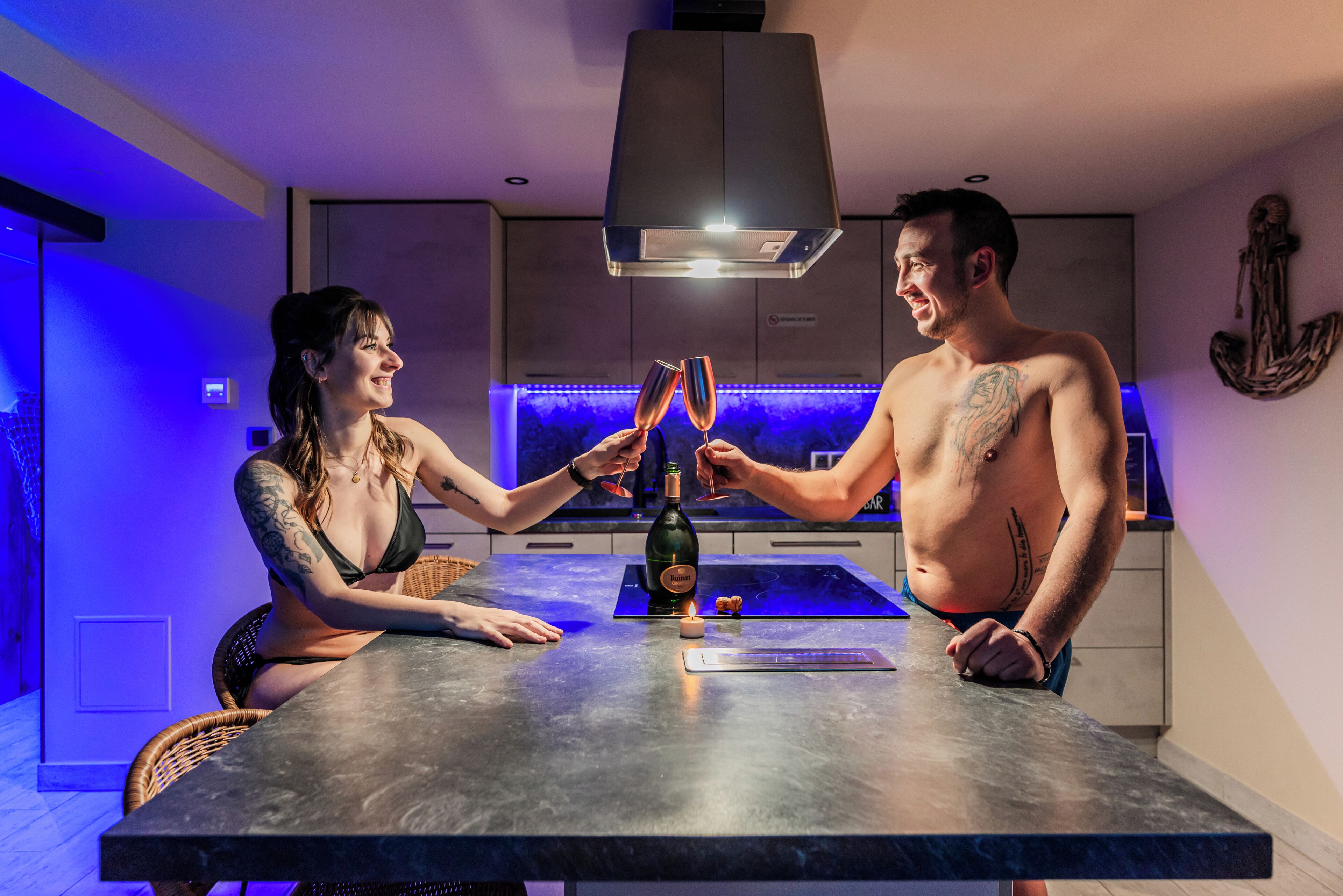 A modern kitchen with a dark countertop, a bottle of champagne, and a small candle.