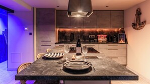 A modern kitchen with a dark marble countertop, two wine glasses, a bottle of wine, and a coffee machine.