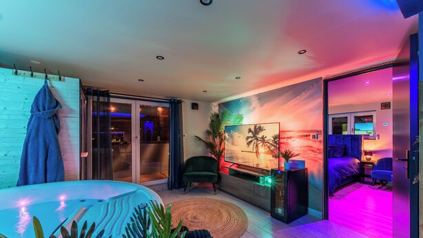 A modern living room with a large painting of a sunset, a cozy seating area, and a view of the ocean through a sliding glass door.