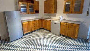 Una cocina con armarios de madera, un refrigerador, un lavavajillas y un piso con estampado de cuadros.