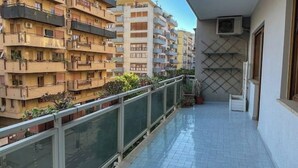 Un balcón con suelo de baldosas, baranda de metal y vistas a edificios de varios pisos.