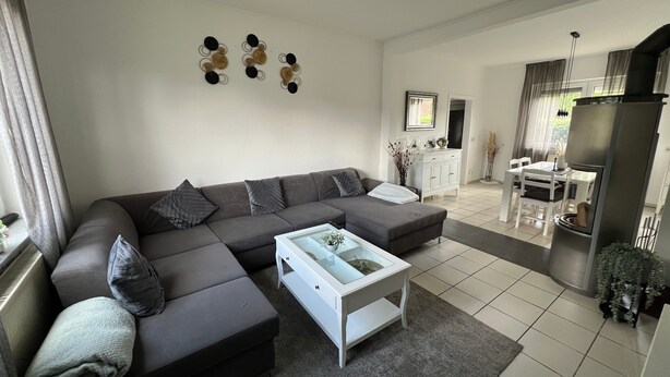 A modern living room with a sectional sofa, a coffee table, and a dining area with a table and chairs. - Holiday Home 'Almir' with Private Terrace, Private Garden and Wi-Fi (Haselünne)