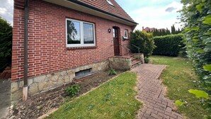 Une maison en briques rouges, avec des fondations en pierre, une porte d’entrée et un petit jardin devant, agrémenté d’un chemin en briques.
