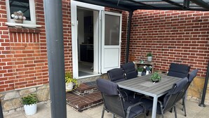 A patio with a table and chairs, a brick wall, a door, and a small garden area. - Holiday Home 'Almir' with Private Terrace, Private Garden and Wi-Fi (Haselünne)