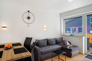 Una sala moderna con un sofá gris, una mesita negra y una mesa de comedor de madera con fruteros.