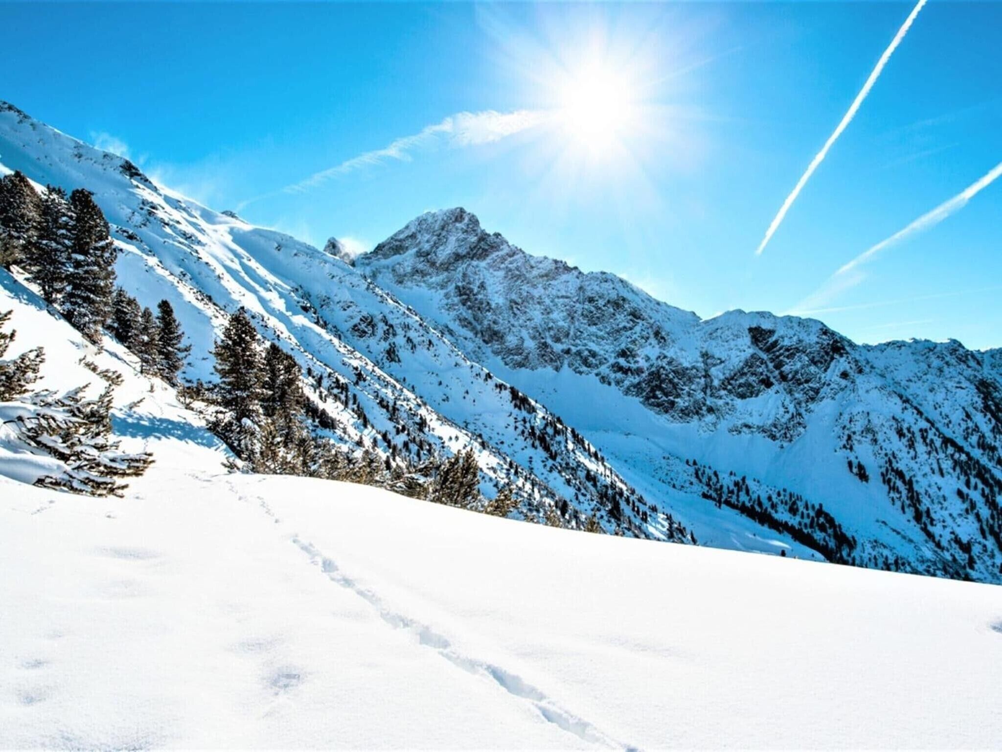 Un paysage montagneux enneigé, avec un ciel dégagé et un soleil éclatant.