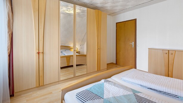 Quarto com uma cama, guarda-roupa de madeira e uma porta.