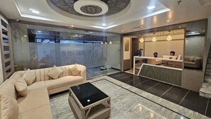 A modern hotel lobby with a sofa, a coffee table, a reception desk, and a patterned ceiling. - Hotel Glorious Grand (Varanasi)