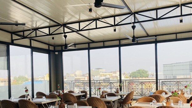 A restaurant with high ceilings, large windows, and a view of the cityscape. - Hotel Glorious Grand (Varanasi)