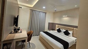 A hotel room with a bed, a desk, a chair, a television, and a window with curtains. - Hotel Glorious Grand (Varanasi)