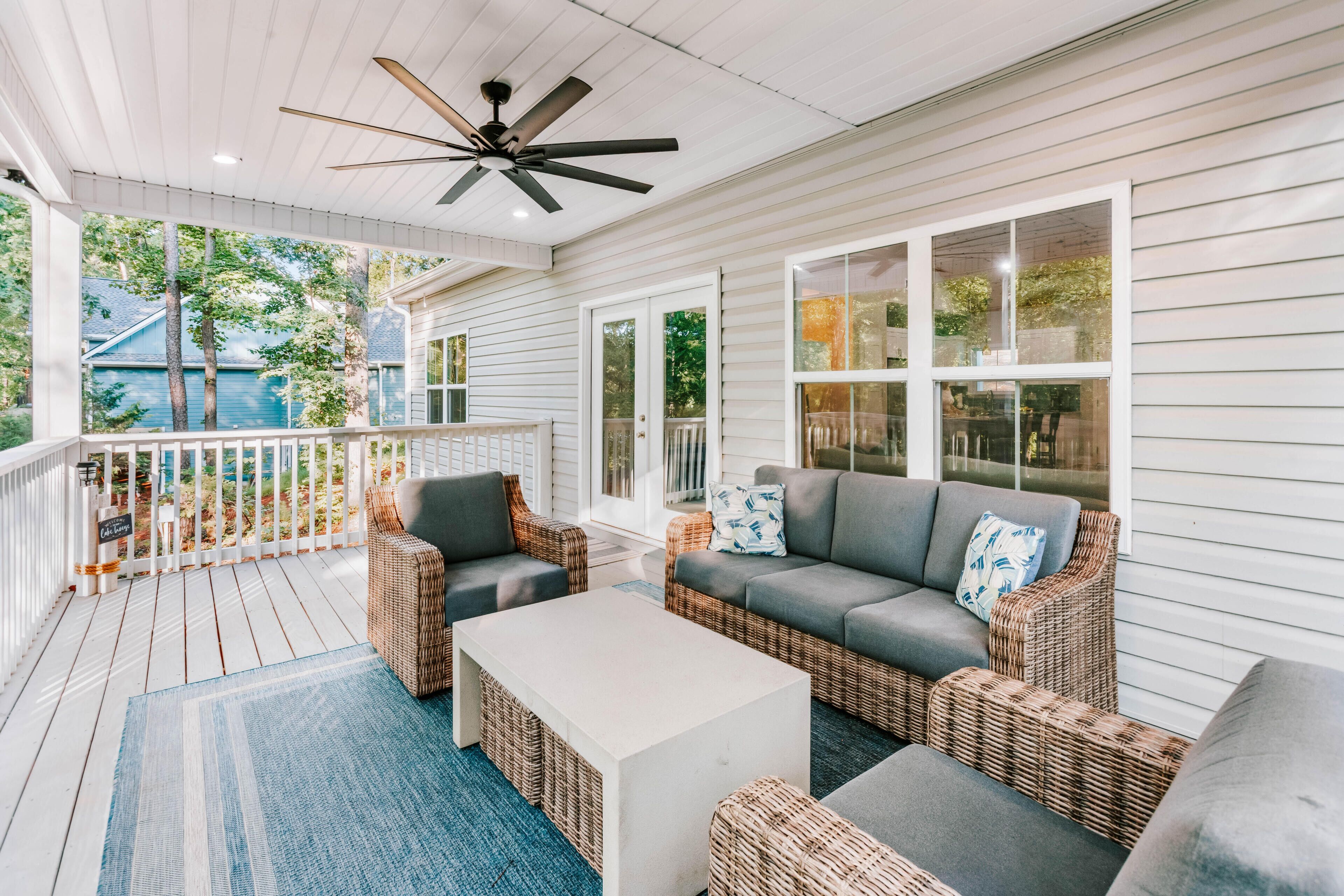 A covered porch with wicker furniture, a ceiling fan, and large windows.