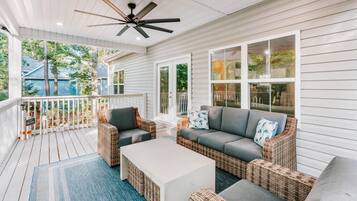 A covered porch with wicker furniture, a ceiling fan, and large windows.