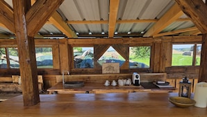 Un intérieur rustique en bois, avec une longue table, un évier et une vue sur l’extérieur.