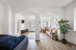 Amplia sala de estar con sofá, mesa de comedor y una planta grande en maceta.