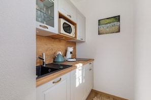 Une cuisine avec un plan de travail en bois, un évier, une bouilloire, un four à micro-ondes et un tableau accroché au mur.