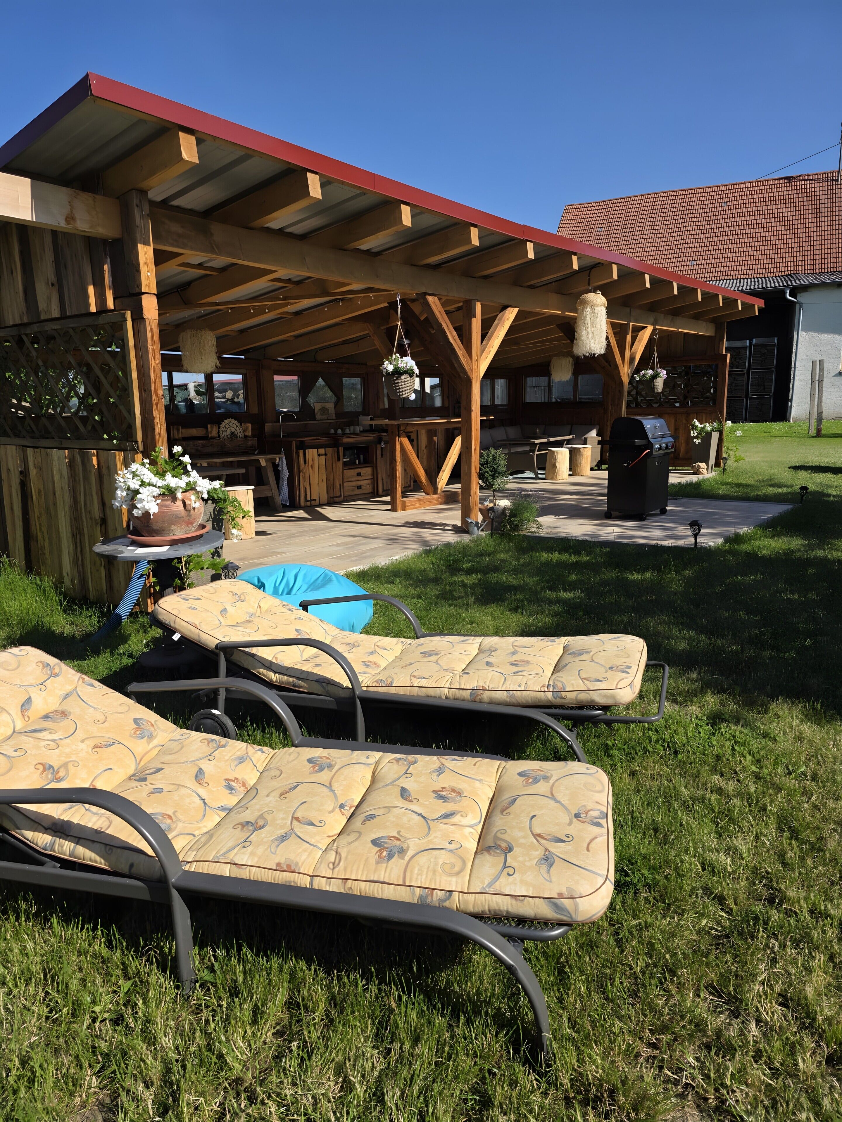 An outdoor patio with a wooden pergola, a barbecue grill, and lounge chairs.