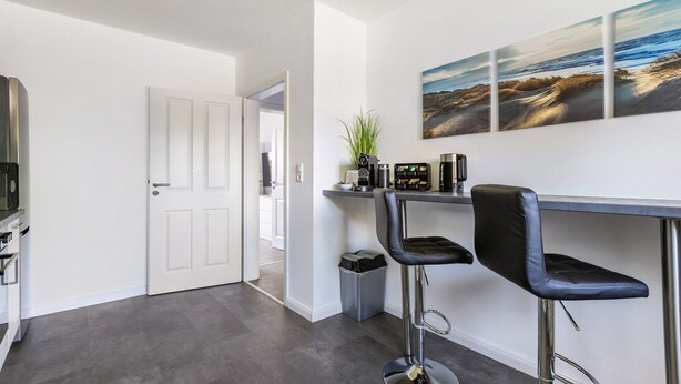 A modern kitchen with a white door, a coffee station, and a view of the beach through the window. - Holiday Home 'Timeout' with Terrace, Garden, Beach Chair & Wi-Fi (Friedrichskoog)