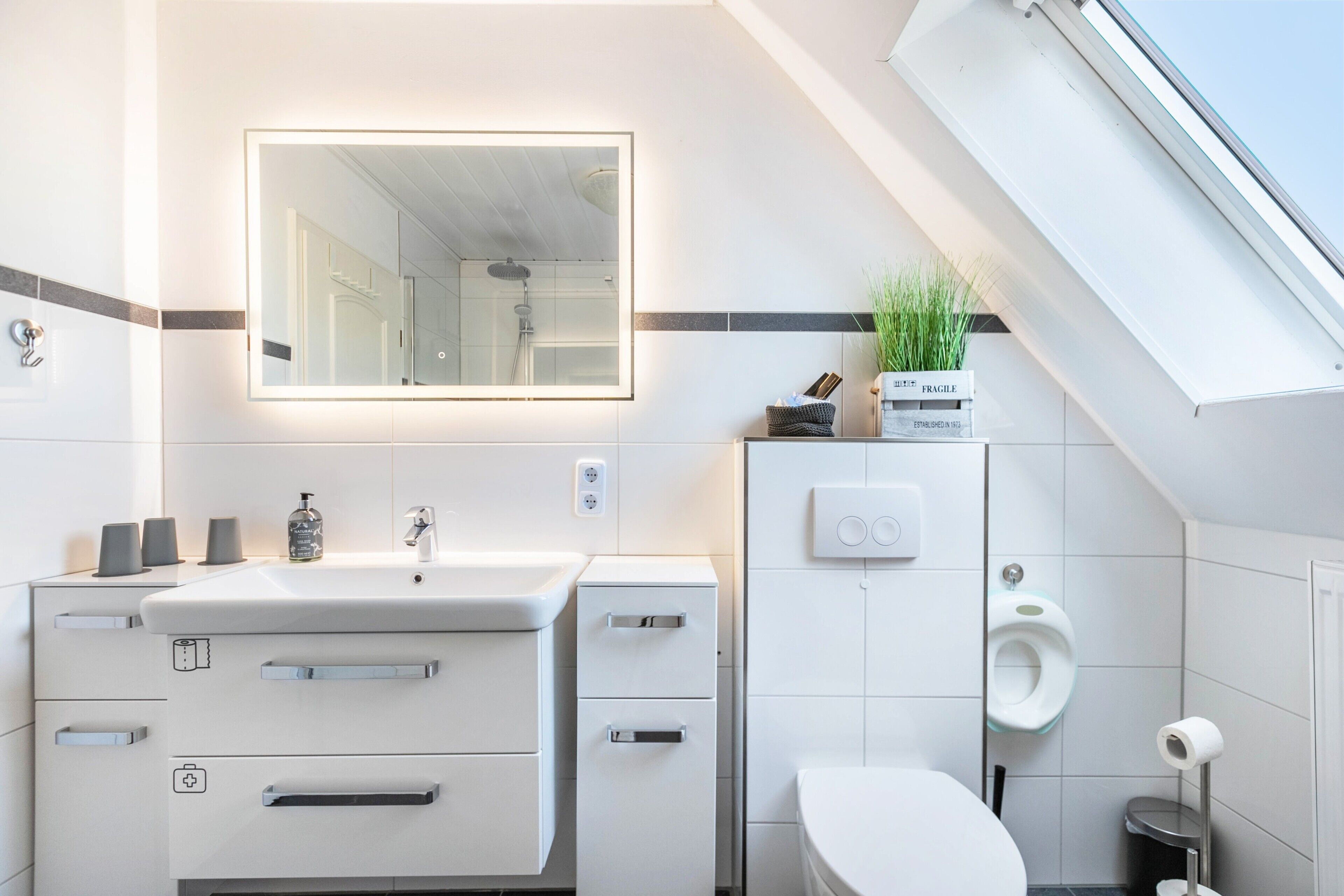 Une salle de bain moderne avec un grand miroir, un lavabo, des toilettes et une petite poubelle.