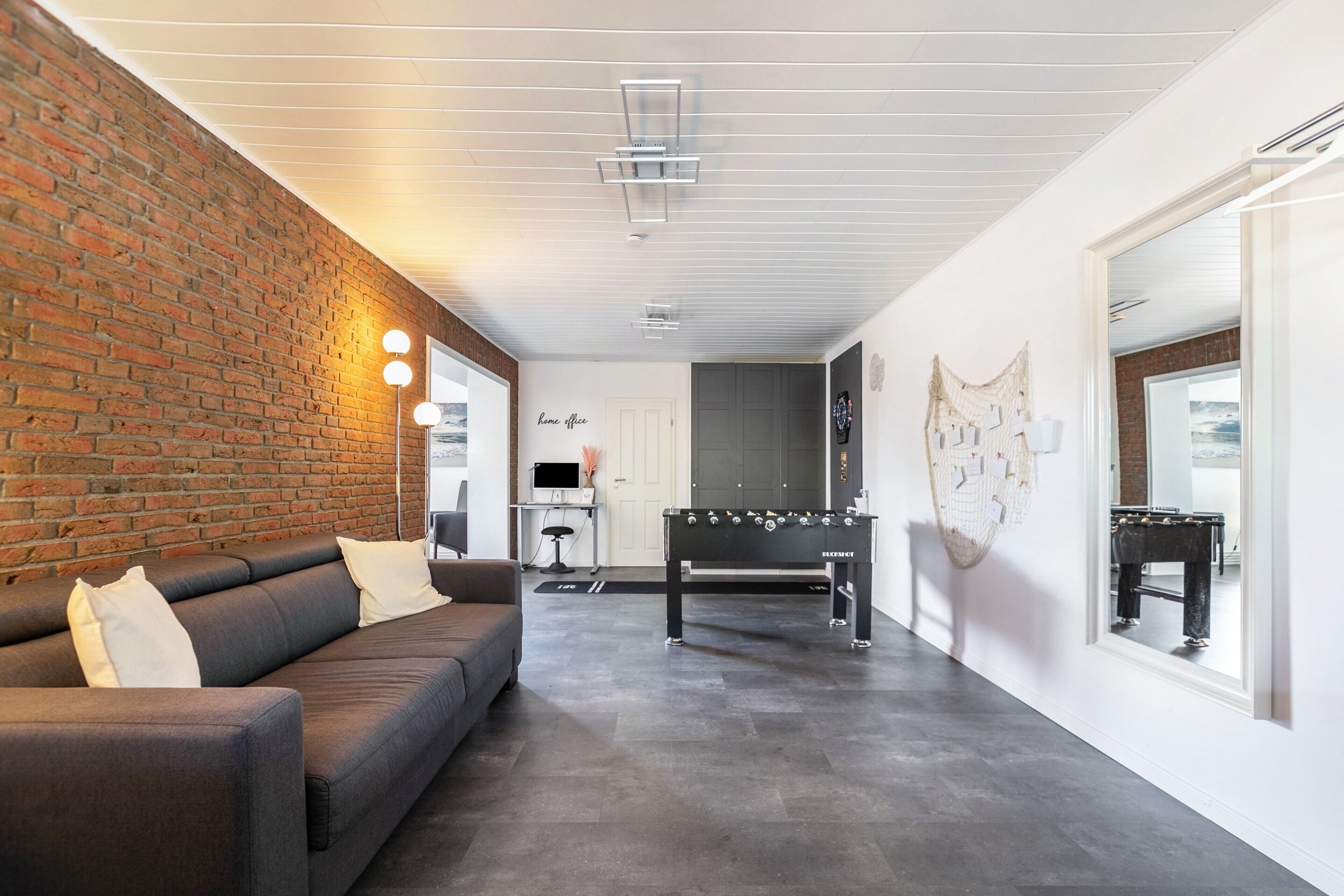 A modern interior with a brick wall, a sofa, a foosball table, and a desk with a computer.