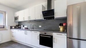 A modern kitchen with white cabinets, stainless steel appliances, a microwave, oven, and a dishwasher. - Holiday Home 'Timeout' with Terrace, Garden, Beach Chair & Wi-Fi (Friedrichskoog)