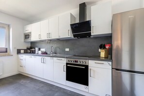 A modern kitchen with white cabinets, stainless steel appliances, a microwave, oven, and a dishwasher. - Holiday Home 'Timeout' with Terrace, Garden, Beach Chair & Wi-Fi (Friedrichskoog)