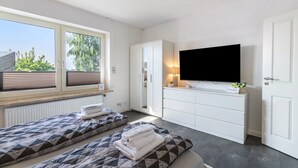 Un dormitorio con dos camas, televisión, cómoda y ventana con persianas.